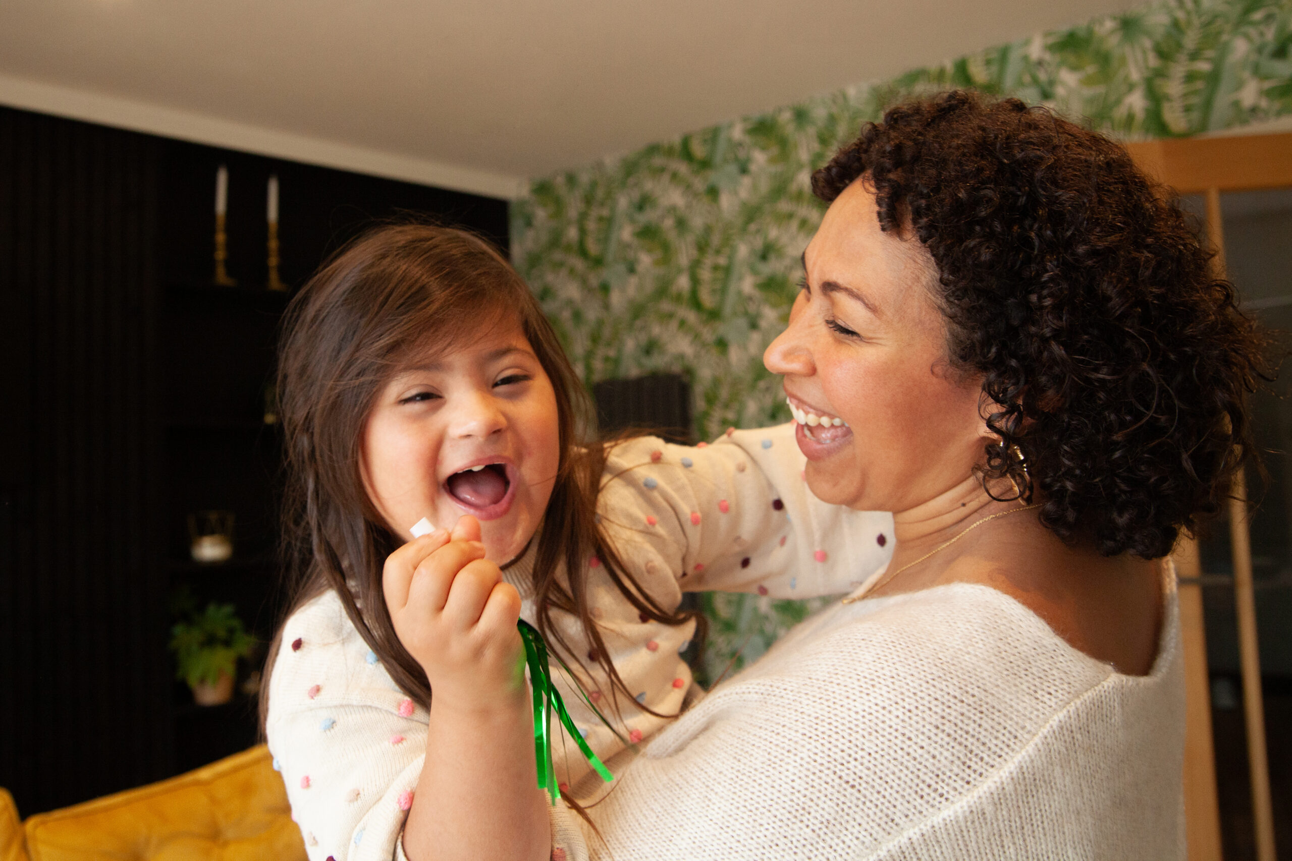 A smiling child with down syndrome is being held by a smiling woman.